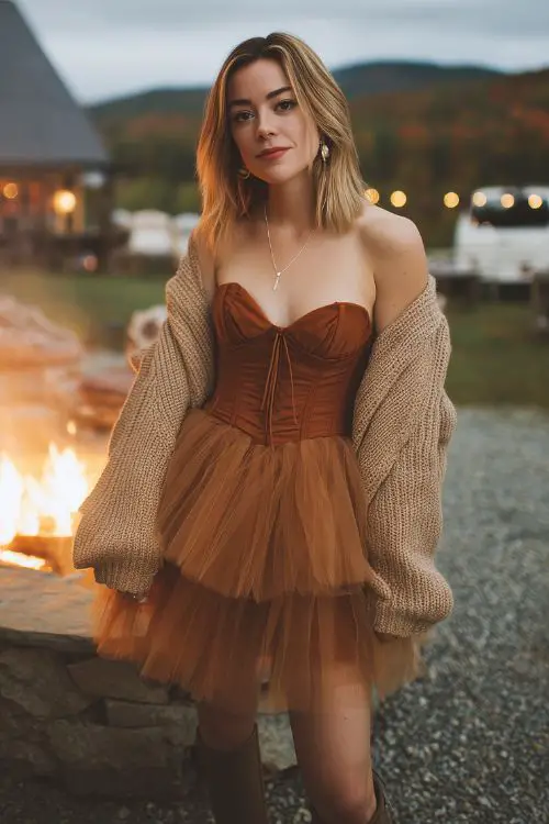A stylish guest wears a cinnamon-colored tulle mini dress with a sweetheart neckline and corset bodice, layered with a cropped knit cardigan