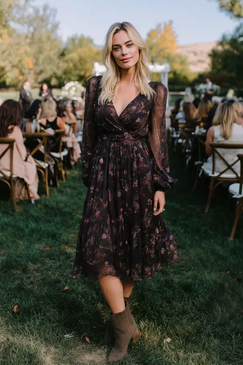 A wedding guest wears a dark floral midi dress with long chiffon sleeves and a cinched waist