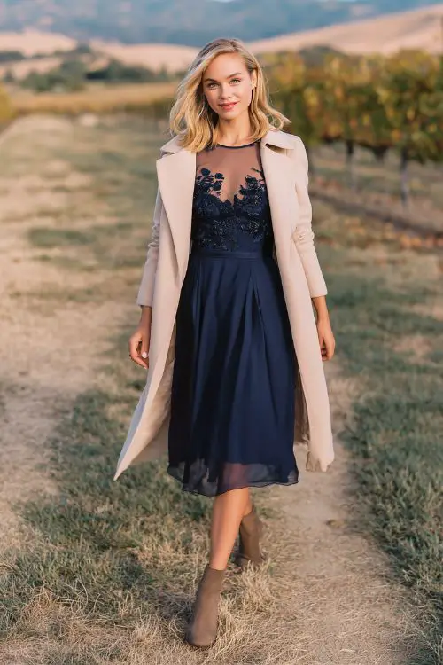 A woman in a navy fit-and-flare dress with embroidered floral accents on the bodice and sheer sleeves