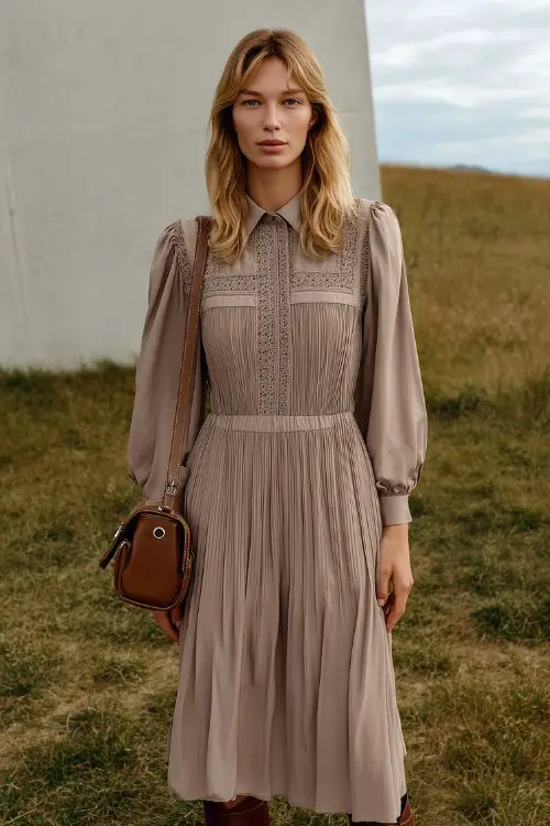 A woman in a soft taupe midi dress with vertical pintuck pleats and a small shoulder bag