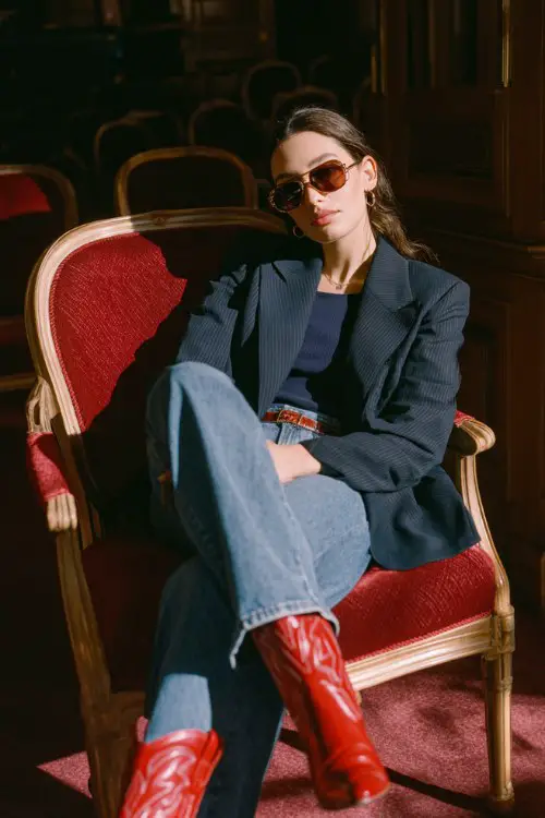 A woman in a tailored navy sport coat high-waisted straight-leg jeans, a navy top and red cowboy boots