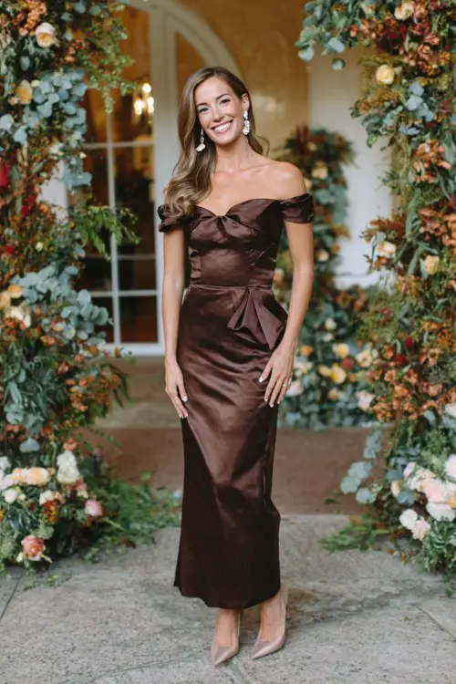 A woman wears a chocolate brown satin gown with an off-shoulder neckline