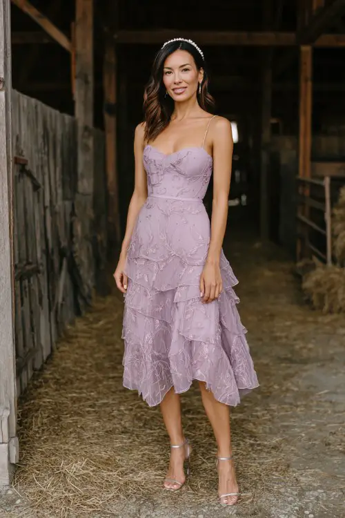 A woman wears a lilac tea-length dress with a fitted bodice and layered chiffon skirt embroidered with silver vines