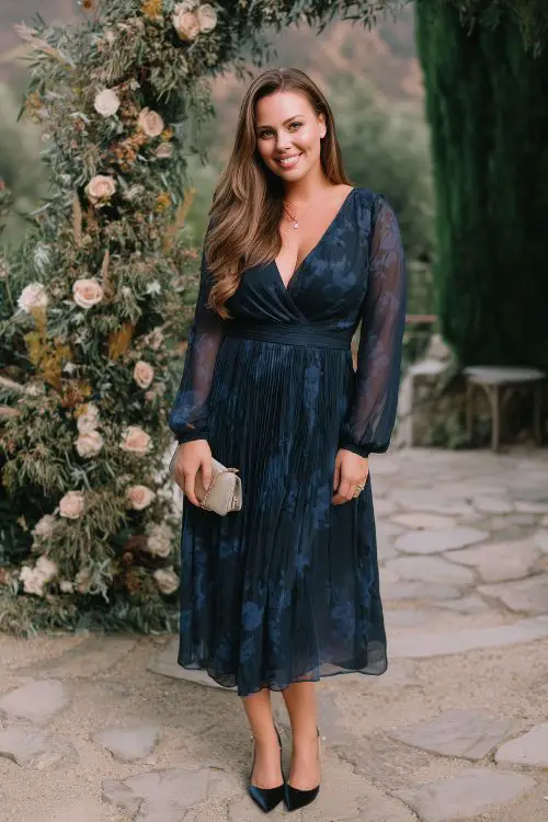 A woman with curves wearing a navy A-line dress with a pleated skirt, long chiffon sleeves, and a subtle floral print 1