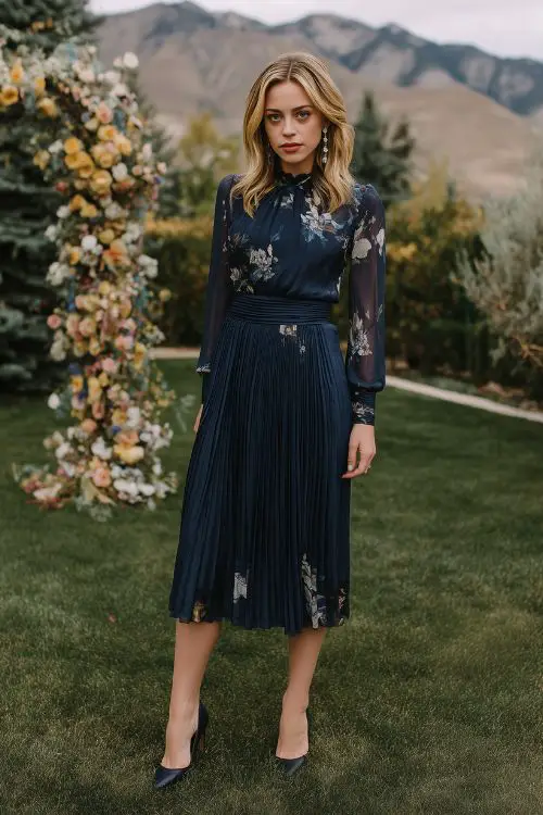 A woman with curves wearing a navy A-line dress with a pleated skirt, long chiffon sleeves, and a subtle floral print