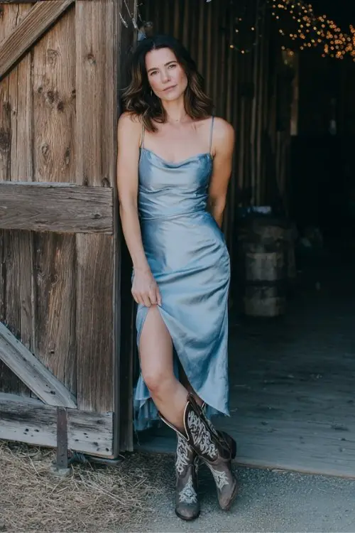Chic country wedding guest outfit with a dusty blue satin slip dress and embroidered cowboy boots