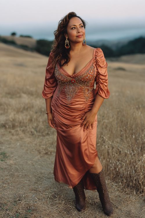 A curvy woman over 40 wears a copper satin gown with draped sleeves and intricate beadwork along the bodice