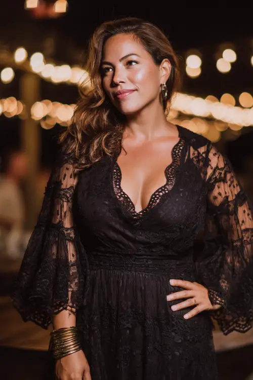 A curvy woman wears a black lace midi dress featuring dramatic bell sleeves, intricate lace embroidery