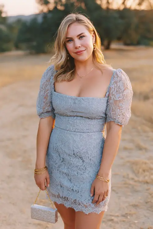 A curvy woman wears a dusty blue short lace dress with soft puff sleeves, and scalloped lace hem detailing
