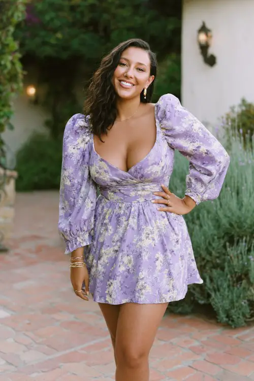 A curvy woman wears a lavender floral mini dress featuring dramatic puff sleeves, a fitted waist, and a flared skater silhouette, styled with block heels