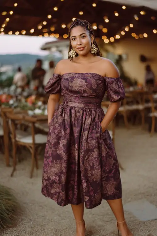 A curvy woman wears a plum floral off-shoulder midi dress with a fitted waist, paired with heeled sandals and bold statement earrings
