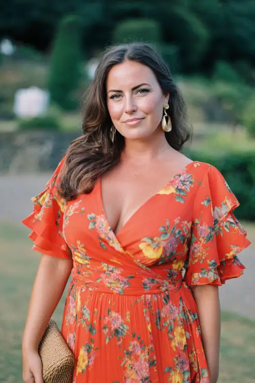 A curvy woman wears a vibrant orange floral wrap dress featuring ruffled sleeves, a flowing chiffon skirt