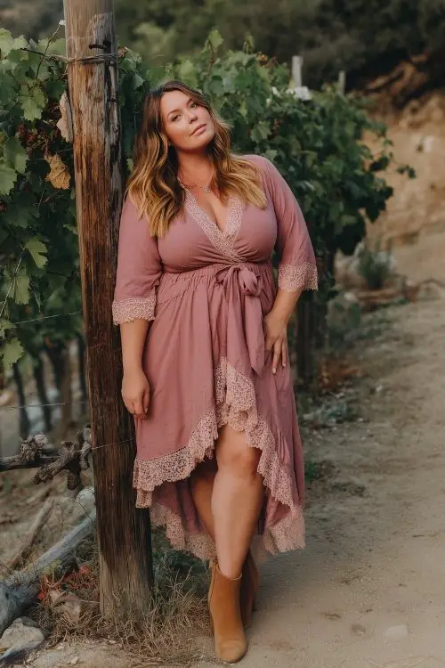 A plus-size woman wears a dusty rose high-low dress with lace trim and soft tan booties