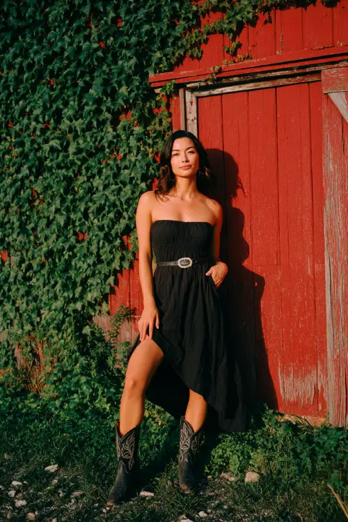 A woman over 30 wears a black high-low casual dress with embroidered cowboy boots and a leather belt