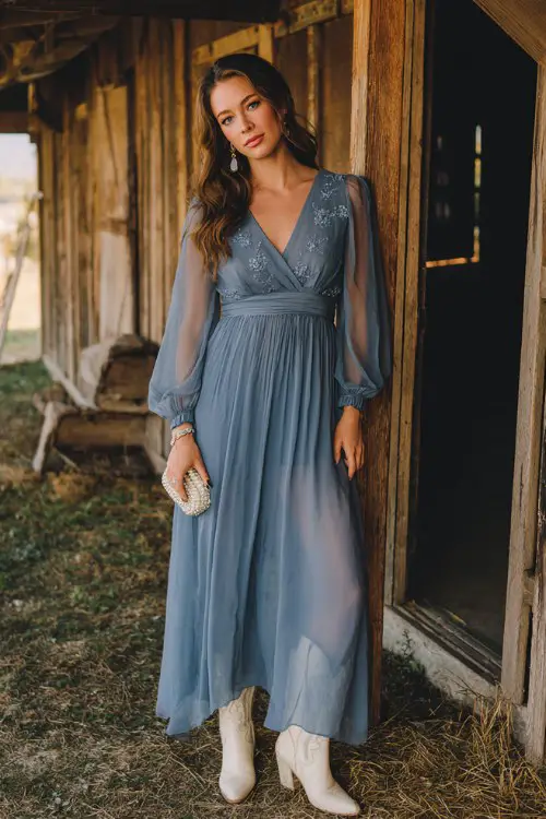A woman over 30 wears a dusty blue chiffon maxi dress with subtle floral appliqués and sheer long sleeves, paired with ivory cowboy boots, a pearl clutch