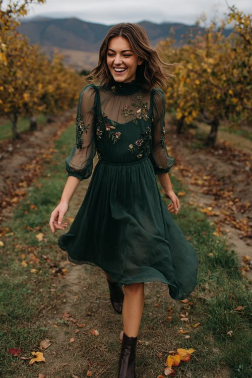 A woman over 30 wears a forest green high-neck dress with sheer sleeves covered in embroidered wildflowers, styled with dark leather ankle boots