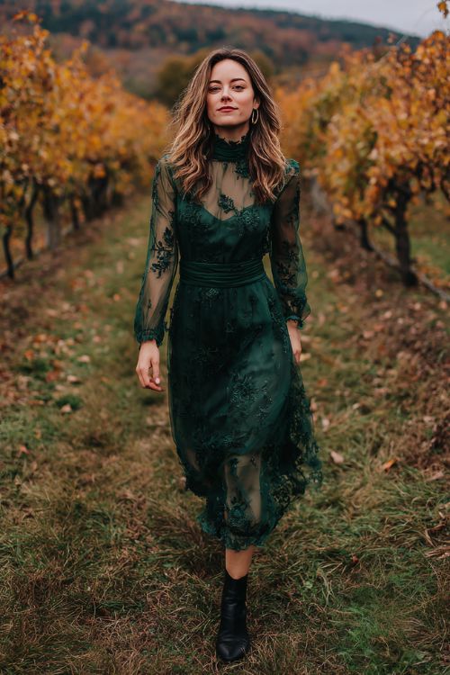 A woman over 30 wears a forest green high-neck dress with sheer sleeves covered in embroidered wildflowers, styled with dark leather ankle boots