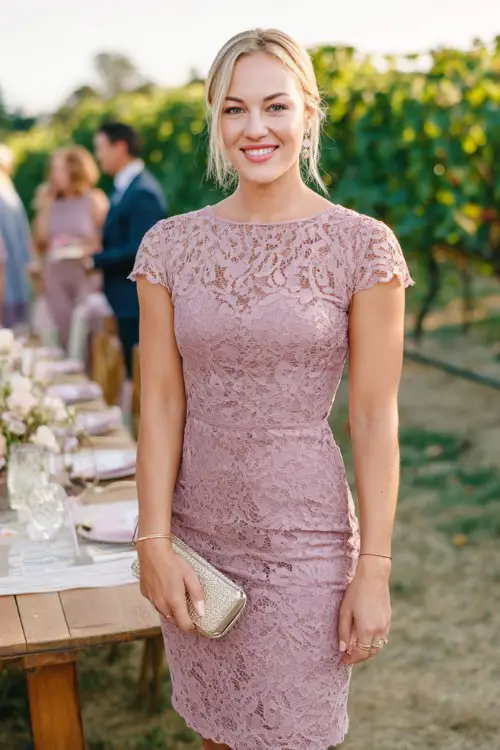 A woman over 30 wears a mauve lace shift dress with cap sleeves, delicate lace overlay, and a straight elegant silhouette