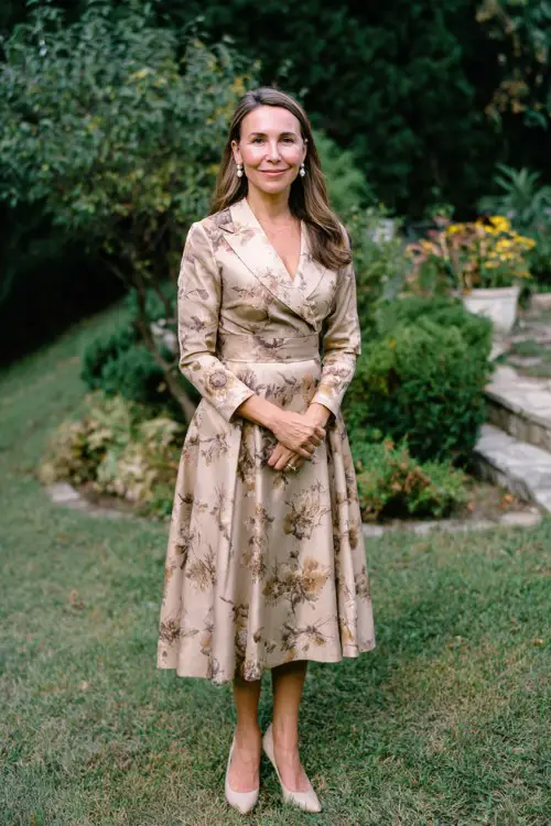 A woman over 40 wears a muted floral A-line midi dress with long sleeves, paired with classic pumps and pearl earrings