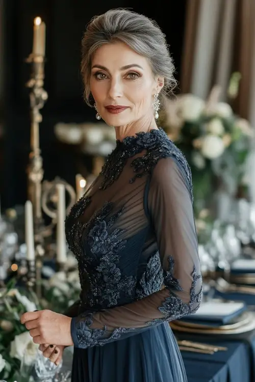 A woman over 50 wears a navy blue wedding guest dress with sheer lace bodice and sleeves