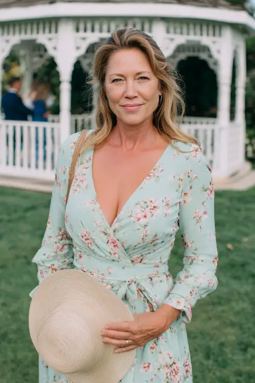 A woman over 50 wears a sleeved mint green floral print dress with a V-neck and subtle peplum waist