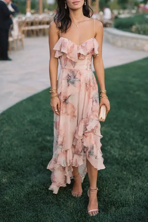 A woman wears a blush floral chiffon dress with ruffled straps, a sweetheart neckline, and a layered ruffle skirt that adds movement