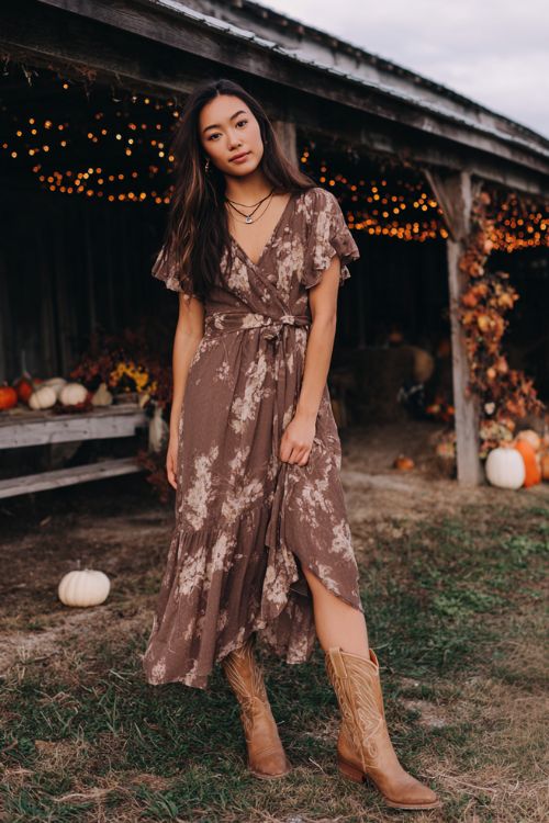 A woman wears a chocolate brown floral chiffon dress with ruffled sleeves and a flowing tiered skirt, styled with caramel cowboy boots