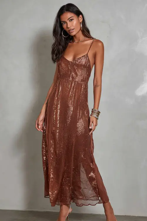 A woman wears a copper sequin slip dress with delicate straps and a flowing chiffon overlay that shimmers in movement