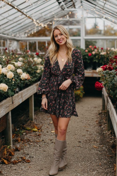 A woman wears a dark floral chiffon dress with flowing sleeves and sleek taupe knee high boots, accessorized with a delicate gold necklace