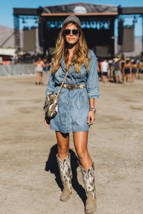 A woman wears a denim mini dress with a belt, cowhide-print cowboy boots
