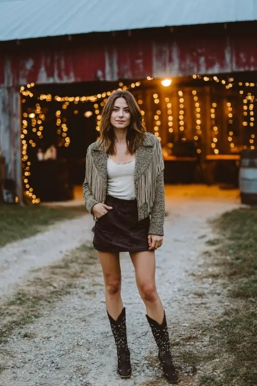 A woman wears a leather mini skirt, a fringed jacket, and studded cowboy boots