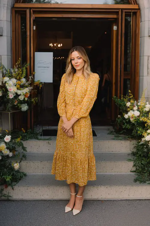 A woman wears a marigold block-print tiered midi with flutter sleeves and covered buttons, paired with ivory Mary Jane heels (2)