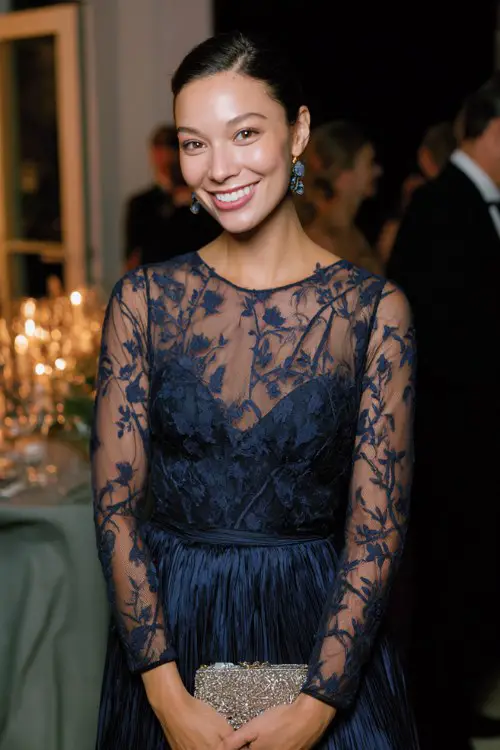 A woman wears a navy lace midi dress featuring delicate vine embroidery, sheer long sleeves, and a flowing pleated skirt that moves gracefully