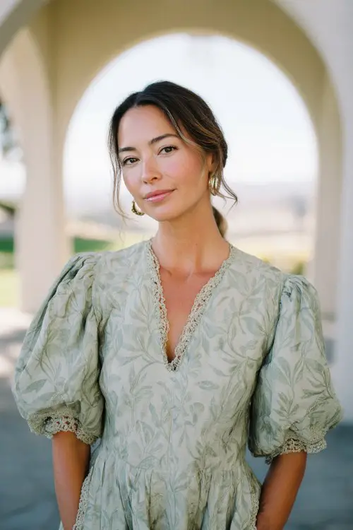 A woman wears a pale sage green dress with a subtle leaf print and lace-trimmed sleeve