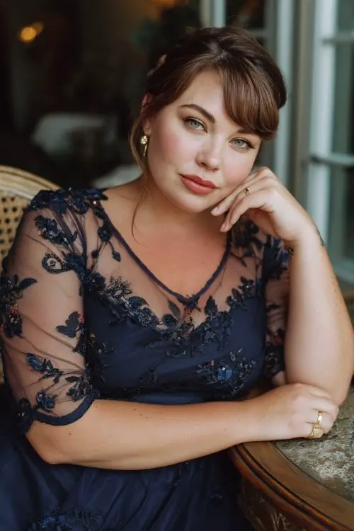 a plus size woman in a navy A-line dress with sheer sleeves and floral embroidery