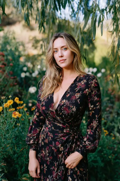 a woman in a black floral print wrap gown with hints of burgundy and gold, standing in a coastal garden