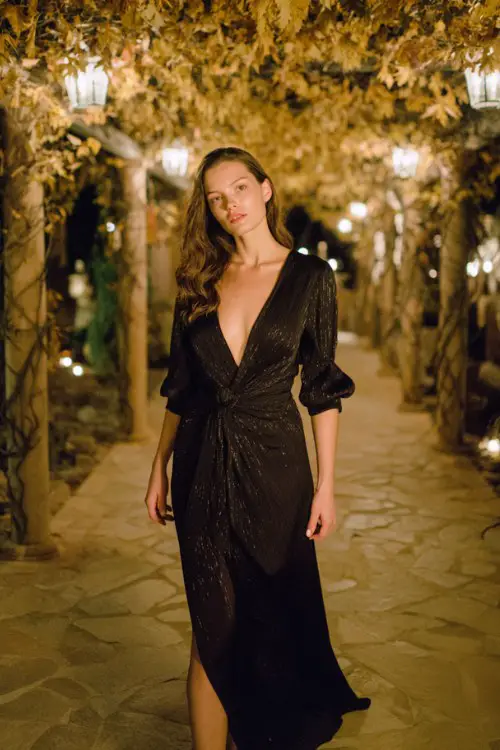 a woman in a black wrap maxi dress with subtle metallic thread accents, standing under a wedding pergola