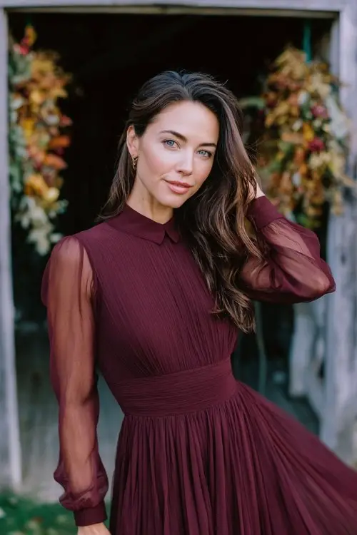 a woman in a burgundy fit-and-flare dress with pleated skirt and sheer long sleeves