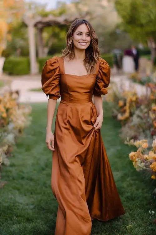 a woman in a copper-colored satin dress with puff sleeves and flowing skirt
