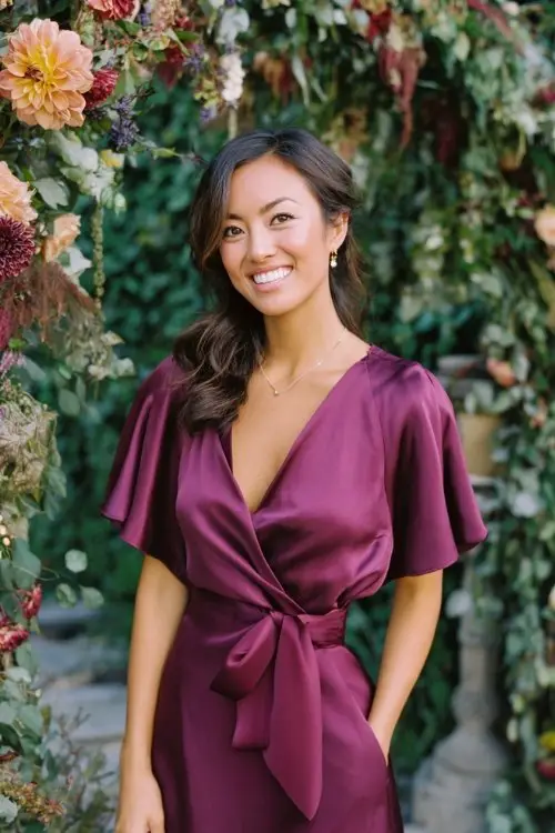 a woman in a deep plum satin knee-length wrap dress with flutter sleeves and a waist tie