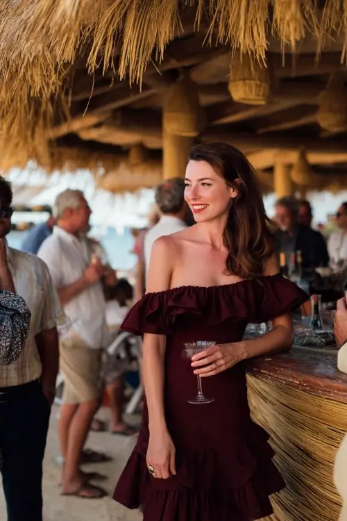 a woman in a deep wine off-shoulder midi dress with a ruffled hem, chatting with guests