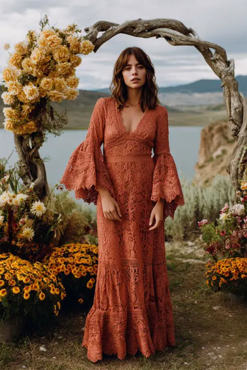 a woman in a terracotta bohemian lace dress with bell sleeves and scalloped hem, standing beside a driftwood wedding arch