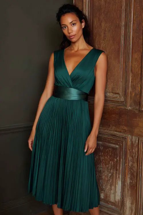 a woman over 30 in a pine green pleated midi dress with satin waistband
