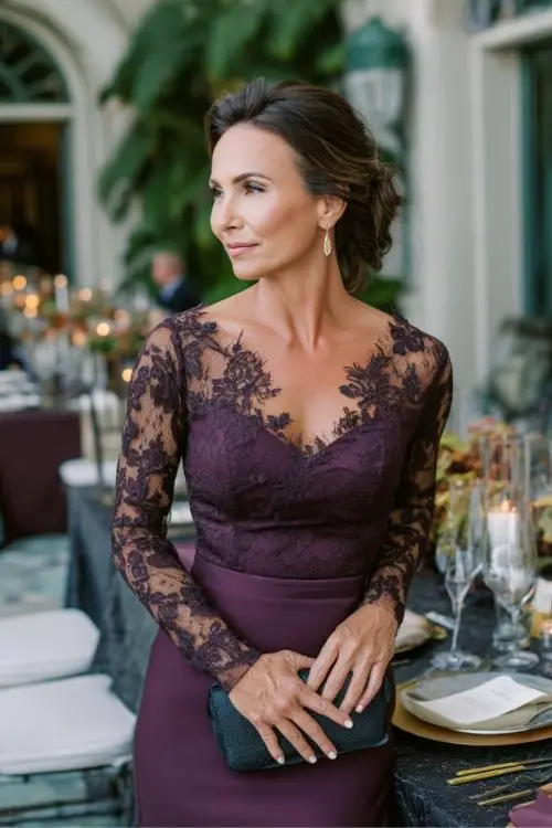 a woman over 50 in a dark plum long-sleeve gown with lace bodice, holding a clutch near a candlelit reception table