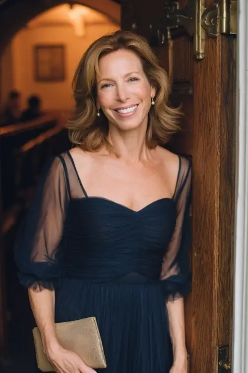 a woman over 50 in a navy chiffon gown with sheer sleeves, holding a small clutch
