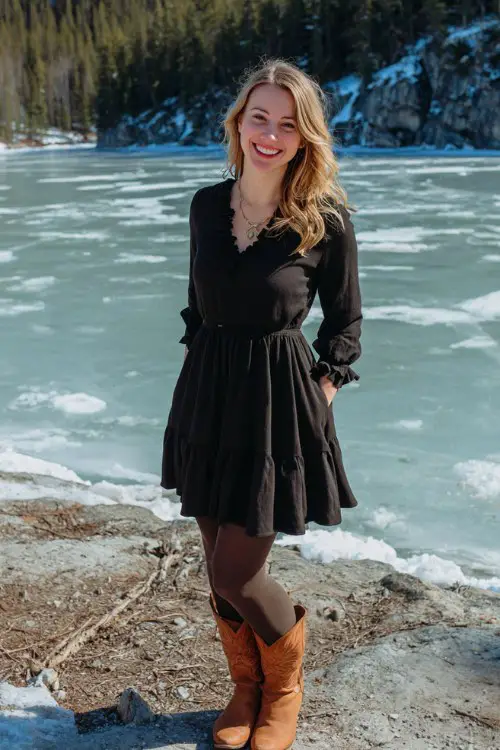 A curvy woman wears a black A-line dress with ruffled cuffs, opaque tights, and brown cowboy boots