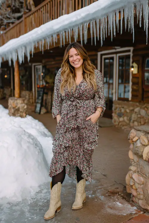 A curvy woman wears a floral midi dress with a ruffle hem, black tights, and beige cowboy boots