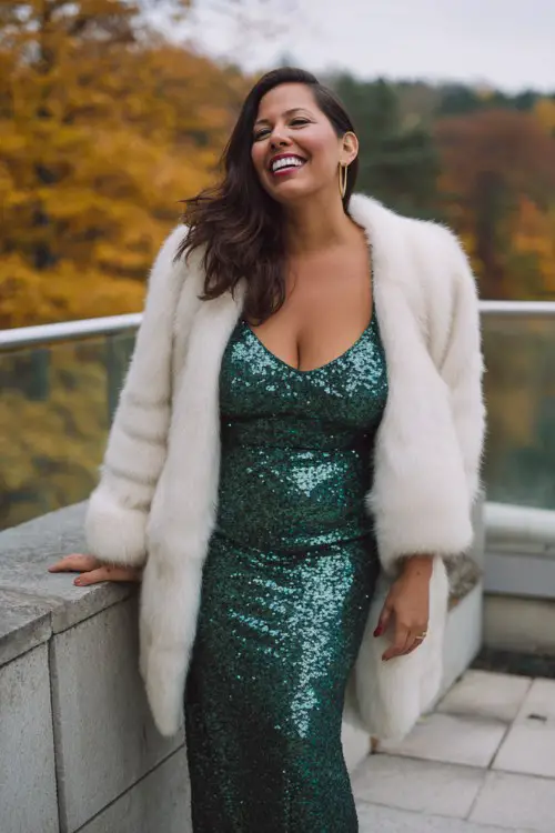 A curvy woman wears a long emerald sequin gown with a white faux fur coat