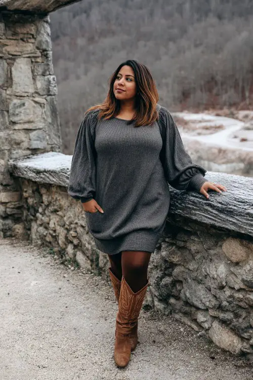 A plus-size woman wears a charcoal-gray sweater dress with bishop sleeves, thick winter tights, and tall brown cowboy boots