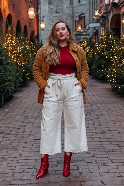 A plus-size woman wears wide-leg cream trousers cropped above red cowboy boots, a ribbed knit top, and a teddy jacket